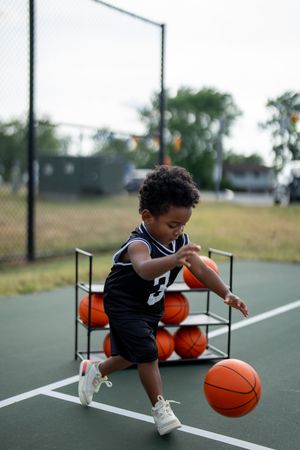 A young child wearing a black jersey plays basketball on an outdoor court, showing energy and focus.